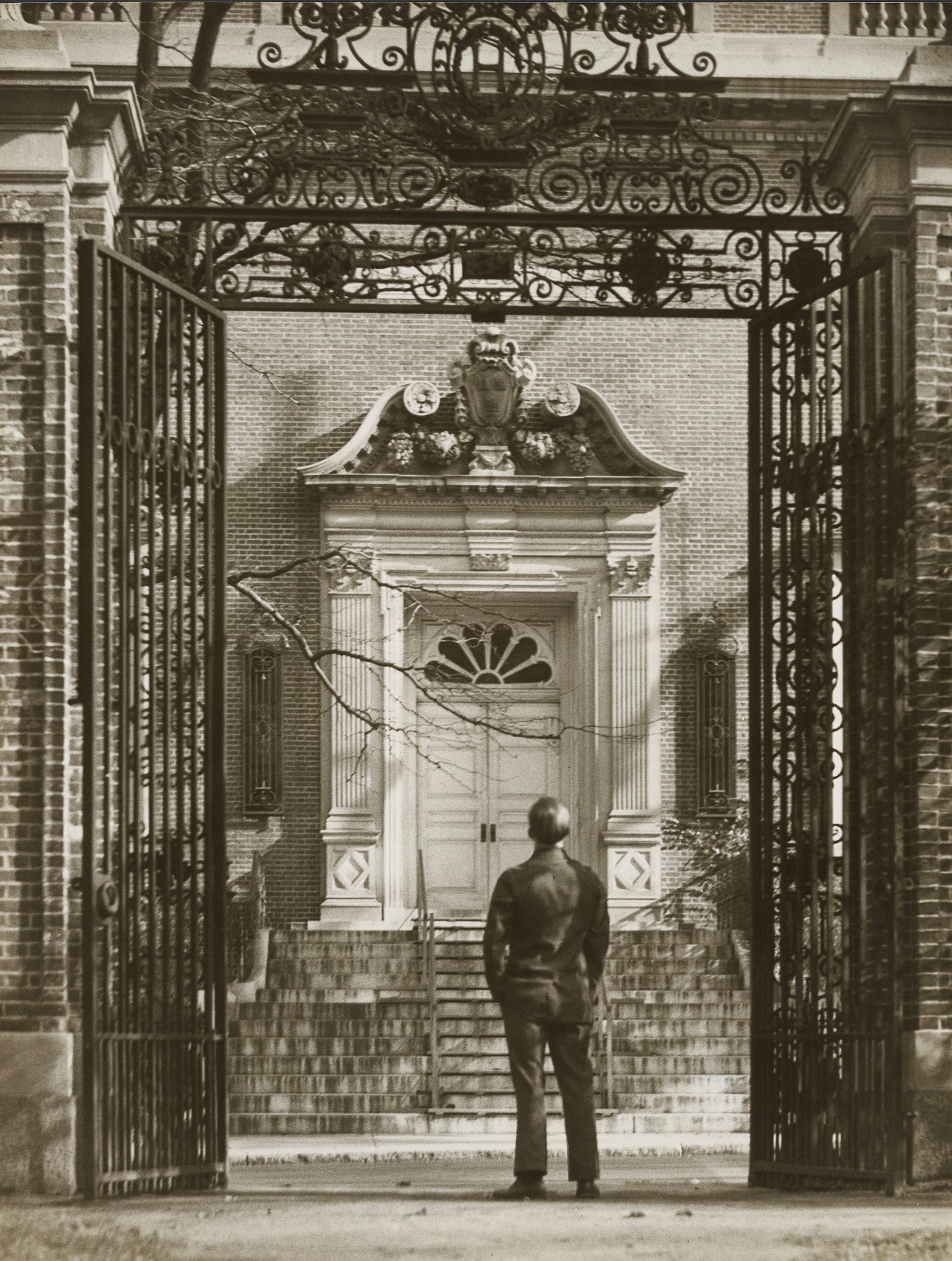 A student standing at an open campus gate, looking up the steps of a college hall.